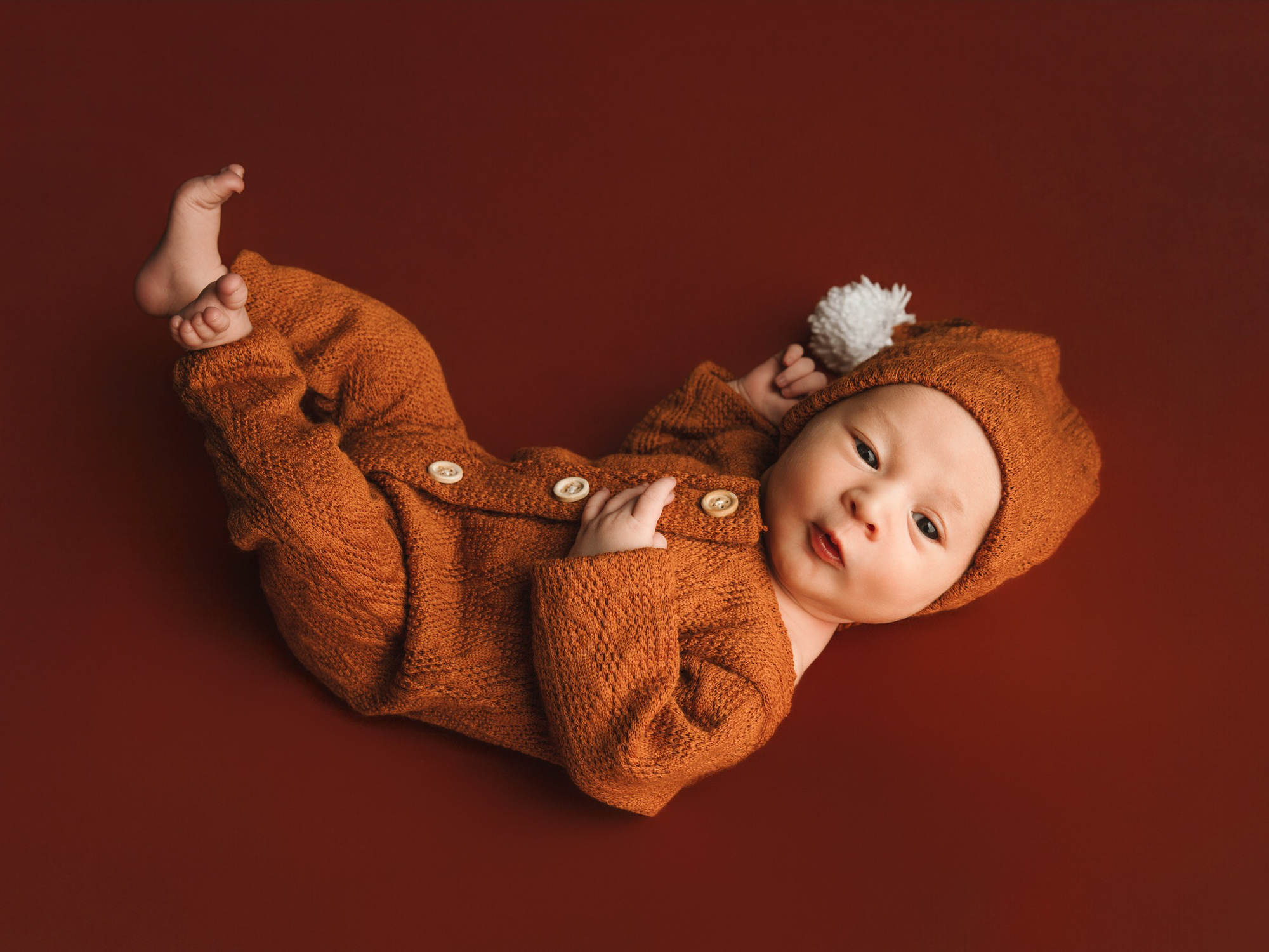 Photographie de naissance minimaliste d'un bébé sur un fond terracotta uni dans notre studio de Mende