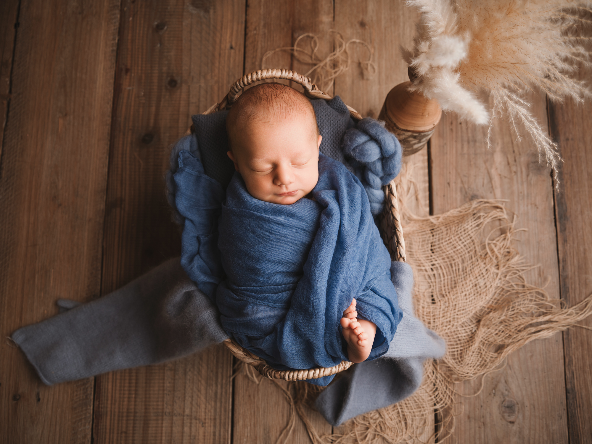 Petit bébé paisiblement endormi dans un petit panier en bois lors d'une séance photo de naissance à Mende