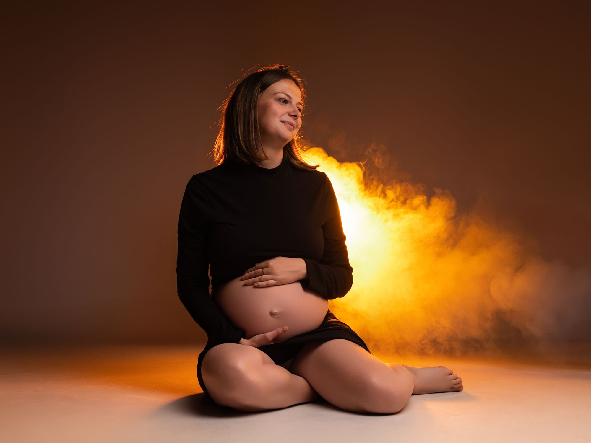 Portrait d'une future maman mettant en valeur son ventre rond dans notre studio à Mende avec de la fumée
