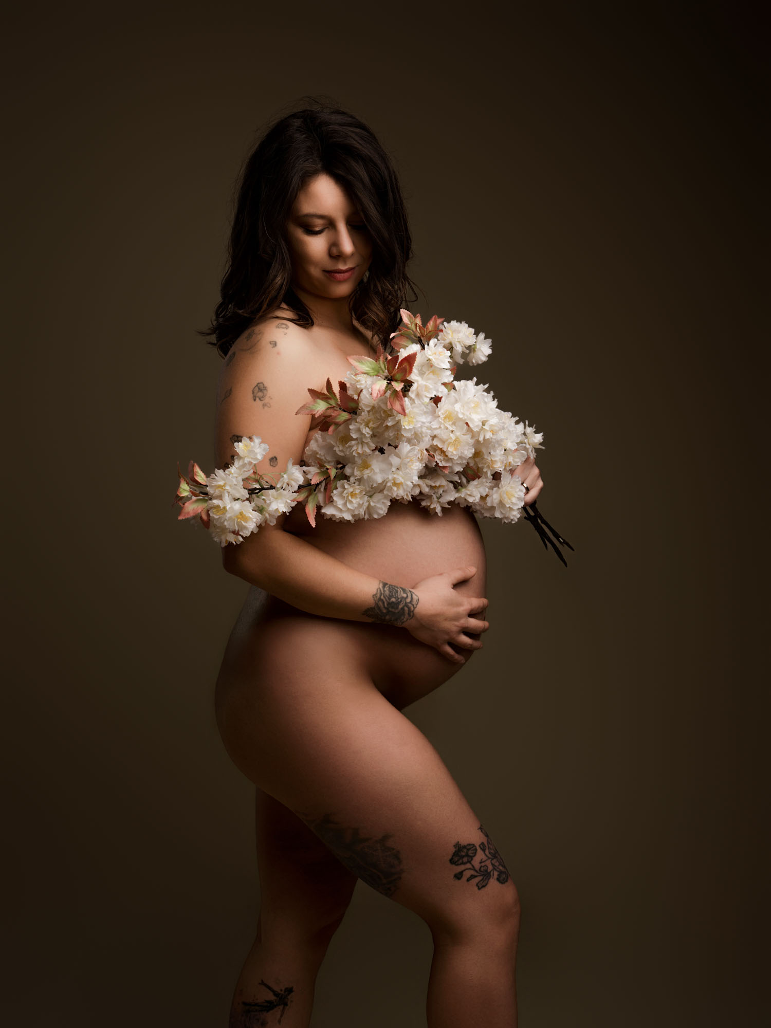 Portrait de profil d'une future maman mettant en valeur son ventre rond dans notre studio à Mende avec des fleurs