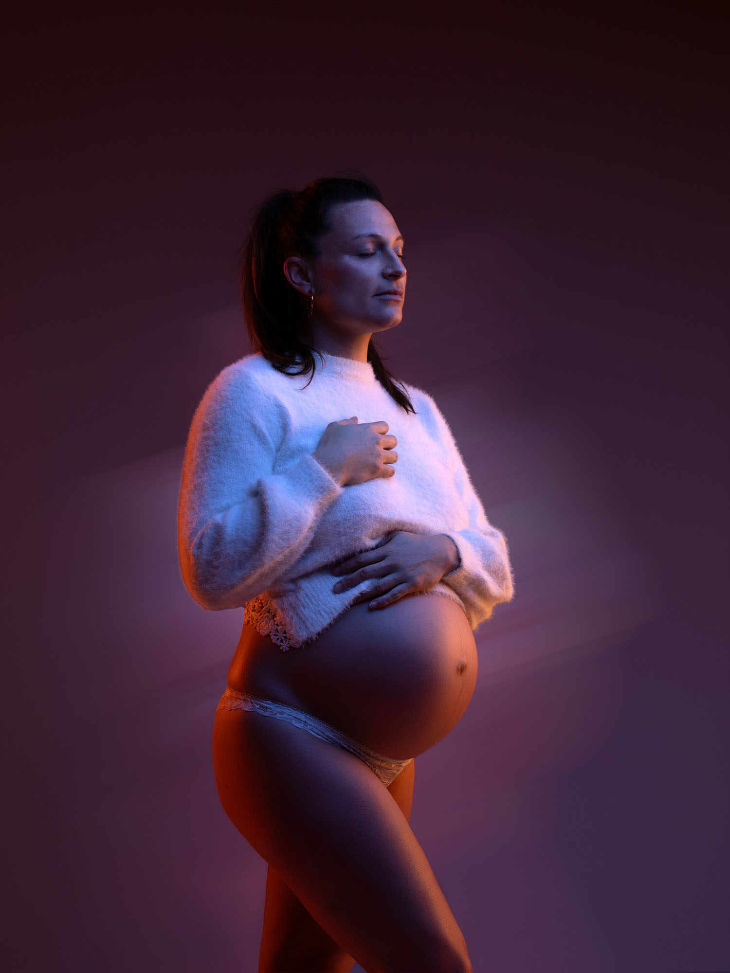 Portrait original d'une future maman éclairée par des lumières colorées de studio à Mende